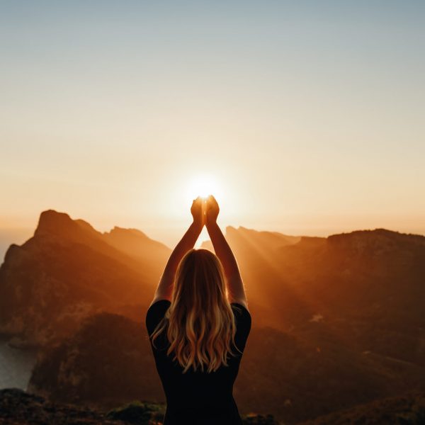 Young woman in spiritual pose holding the light in front of mountains